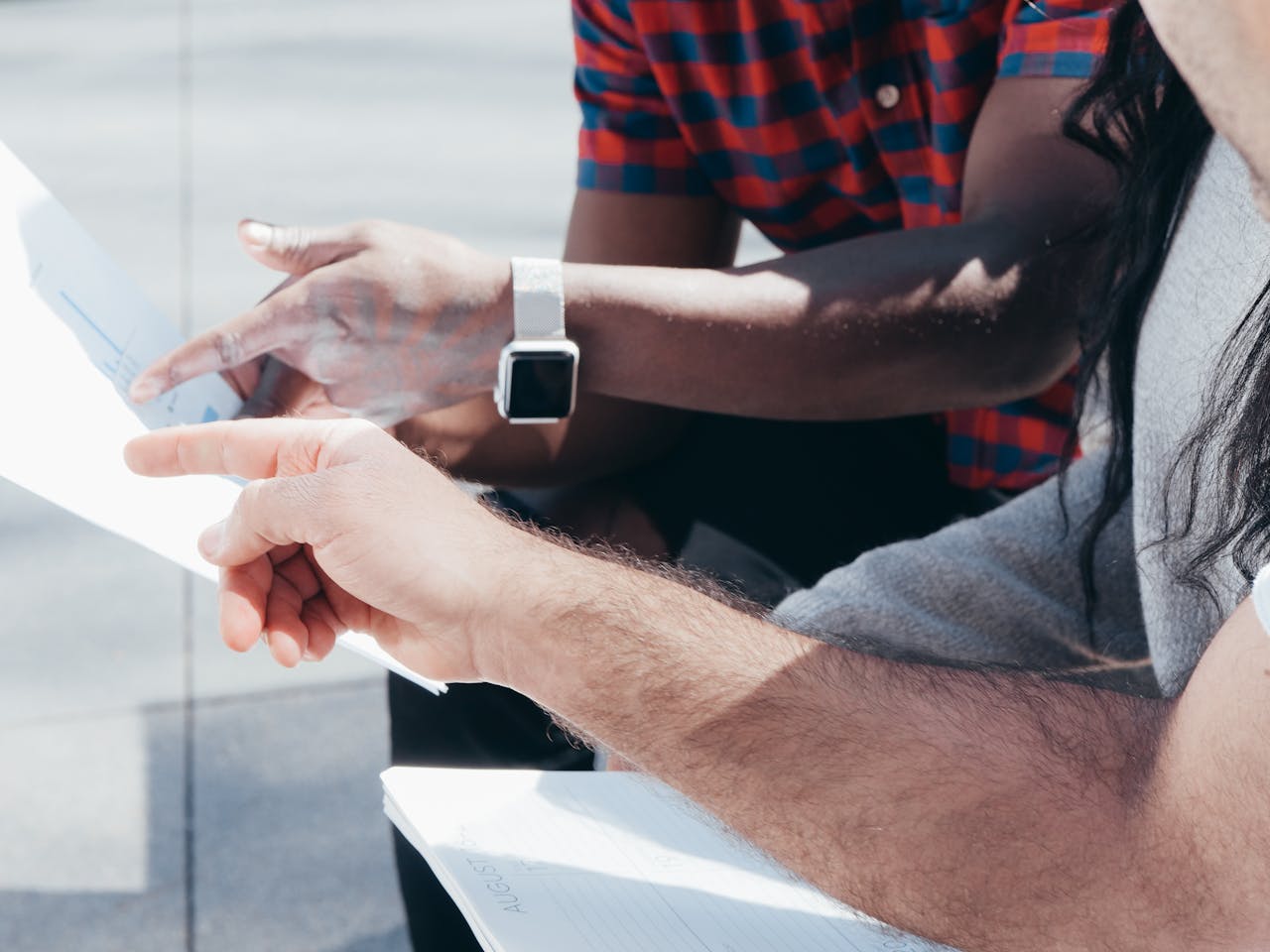 Two people discussing documents with pointing fingers and smartwatch outdoors.